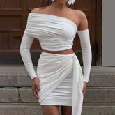 Woman wearing a white off-shoulder dress with long sleeves in front of a wooden door.